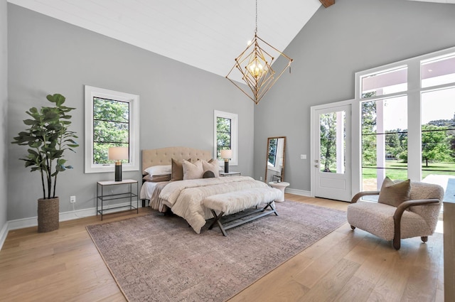 bedroom featuring light wood finished floors, multiple windows, high vaulted ceiling, and an inviting chandelier