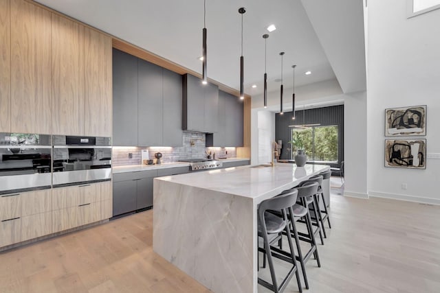 kitchen with tasteful backsplash, modern cabinets, stainless steel oven, and light wood-style floors