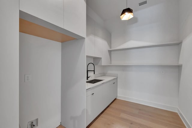 kitchen with light wood finished floors, open shelves, visible vents, white cabinetry, and a sink