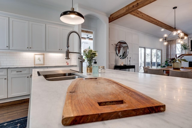 kitchen with beamed ceiling, pendant lighting, a sink, decorative backsplash, and light stone countertops