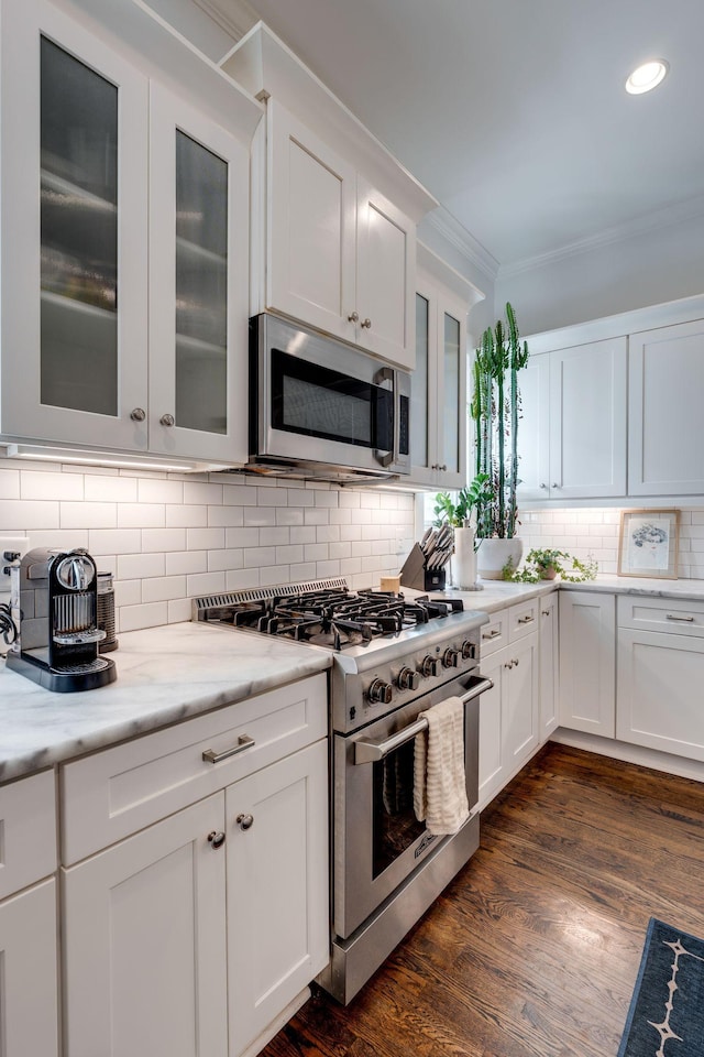 kitchen featuring backsplash, ornamental molding, appliances with stainless steel finishes, white cabinetry, and dark wood-style flooring