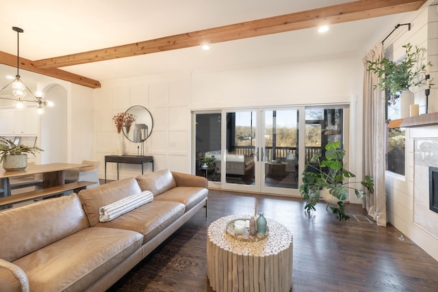 living area with beamed ceiling, an inviting chandelier, a fireplace, a decorative wall, and dark wood-style flooring