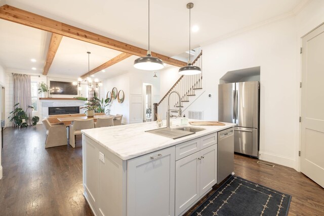 kitchen featuring dark wood finished floors, decorative light fixtures, a glass covered fireplace, stainless steel appliances, and a sink