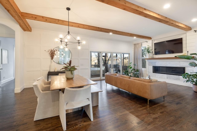 dining room with a glass covered fireplace, dark wood-type flooring, a decorative wall, and beam ceiling