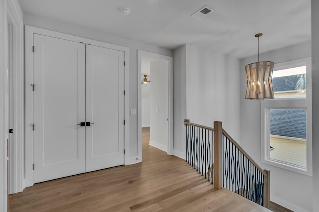 hallway with visible vents, an upstairs landing, wood finished floors, a chandelier, and baseboards