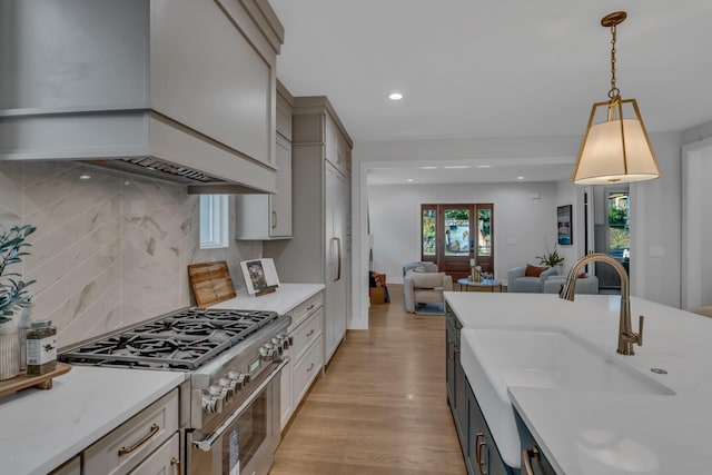 kitchen featuring light wood finished floors, stainless steel stove, open floor plan, a sink, and premium range hood