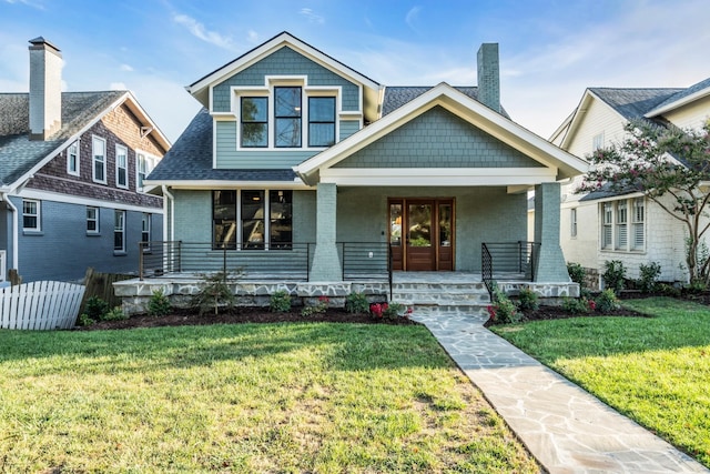 view of front of property featuring covered porch, brick siding, a shingled roof, fence, and a front yard