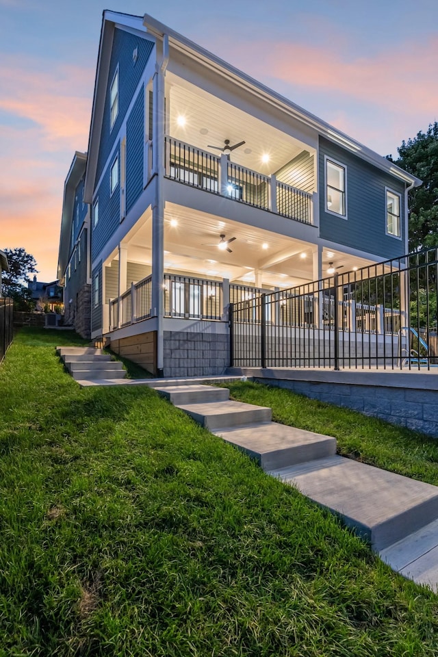 exterior space with a balcony, ceiling fan, fence, and a front yard