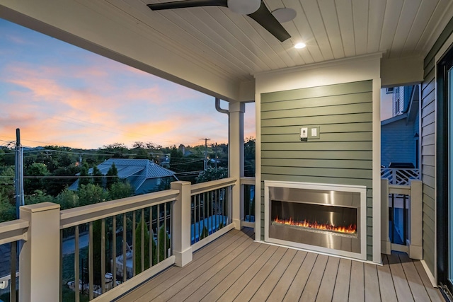 wooden deck featuring a warm lit fireplace and ceiling fan