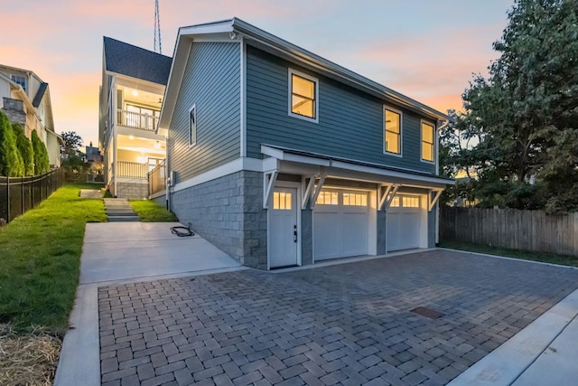 view of front of property featuring decorative driveway, stairway, an attached garage, fence, and a balcony