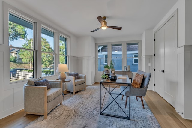 sitting room with ceiling fan, wood finished floors, and a decorative wall