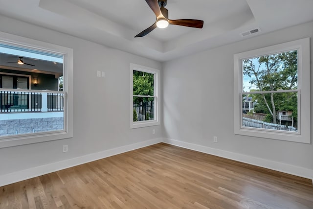 spare room with wood finished floors, a ceiling fan, visible vents, baseboards, and a raised ceiling