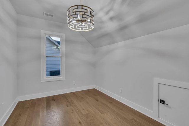 empty room with visible vents, vaulted ceiling, wood finished floors, a chandelier, and baseboards