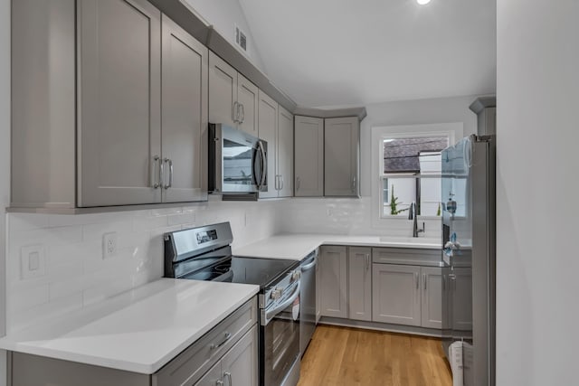 kitchen with light wood finished floors, a sink, gray cabinets, stainless steel appliances, and backsplash