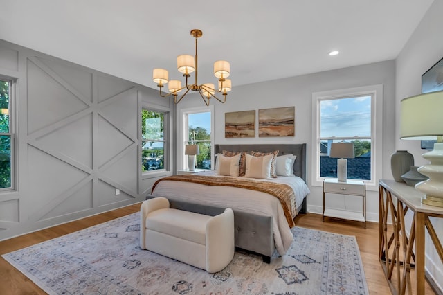 bedroom with multiple windows, a decorative wall, an inviting chandelier, and wood finished floors