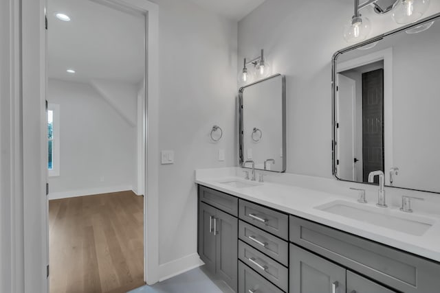 bathroom with double vanity, baseboards, a sink, and wood finished floors