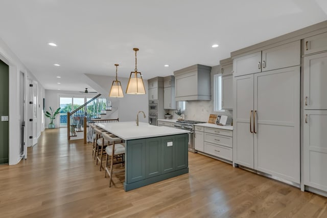 kitchen with a breakfast bar area, high end appliances, light countertops, a kitchen island with sink, and premium range hood