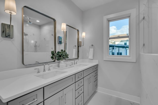 bathroom featuring double vanity, a stall shower, a sink, and baseboards