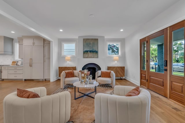 living area with light wood-type flooring, a brick fireplace, baseboards, and recessed lighting