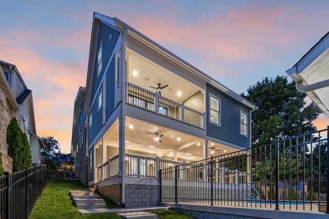 rear view of house featuring a balcony, ceiling fan, fence, and a yard