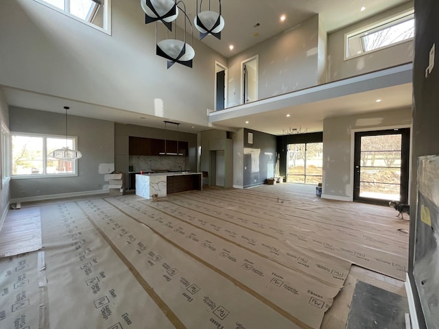 unfurnished living room featuring a high ceiling, an inviting chandelier, a wealth of natural light, and baseboards