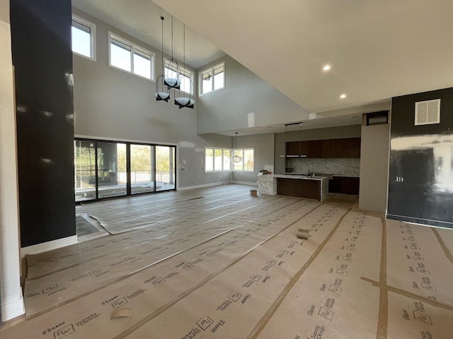 unfurnished living room with a chandelier, recessed lighting, a towering ceiling, visible vents, and baseboards