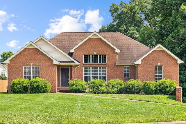 traditional-style house with a shingled roof, a front yard, and brick siding