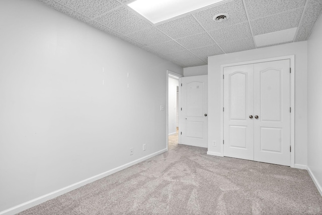 unfurnished bedroom featuring visible vents, baseboards, a drop ceiling, carpet, and a closet