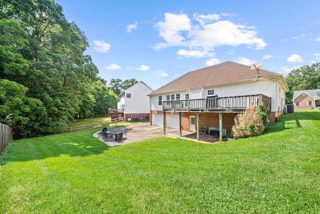 rear view of property with a deck, concrete driveway, a lawn, and a patio area