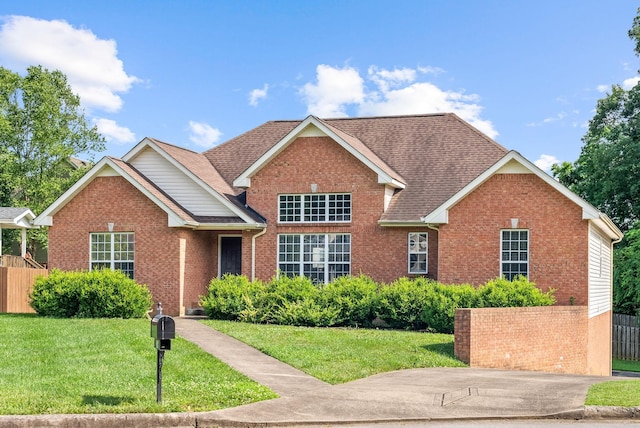 traditional home with a shingled roof, a front yard, brick siding, and fence