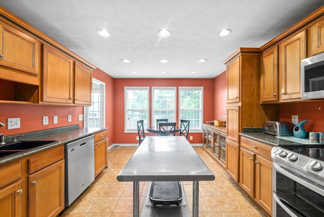 kitchen with light tile patterned floors, appliances with stainless steel finishes, brown cabinets, and a sink