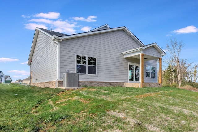 back of house with central AC unit, a lawn, and brick siding