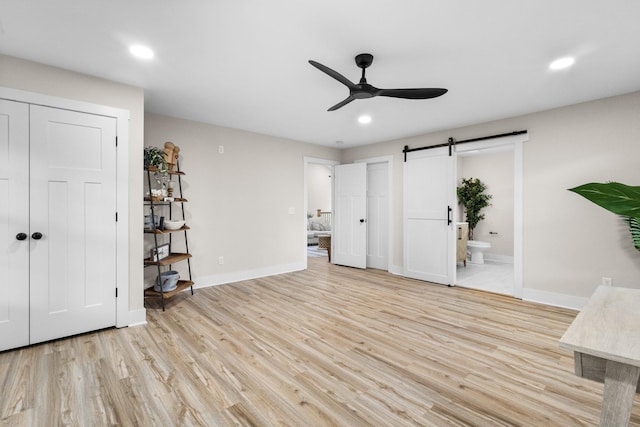 interior space with light wood-type flooring, a barn door, baseboards, and a ceiling fan