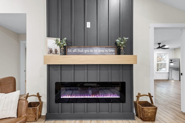 details featuring a ceiling fan, a large fireplace, and wood finished floors