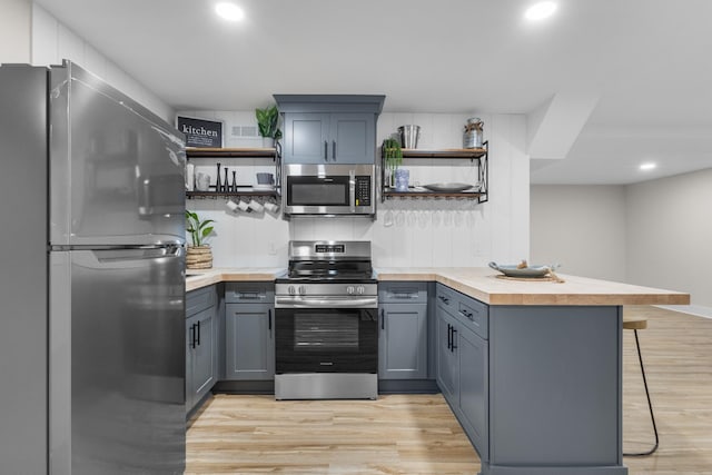 kitchen with open shelves, appliances with stainless steel finishes, light wood-type flooring, and a peninsula