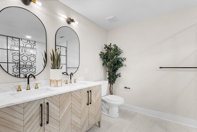 bathroom with toilet, double vanity, baseboards, and a sink