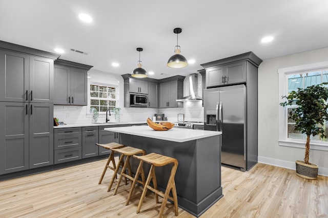 kitchen featuring stainless steel appliances, light countertops, backsplash, a sink, and wall chimney range hood