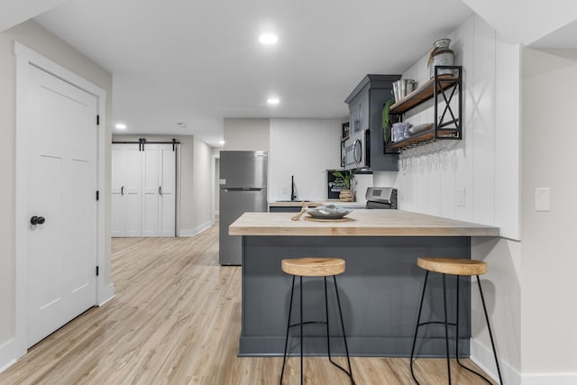 kitchen featuring a barn door, a peninsula, appliances with stainless steel finishes, open shelves, and a kitchen bar