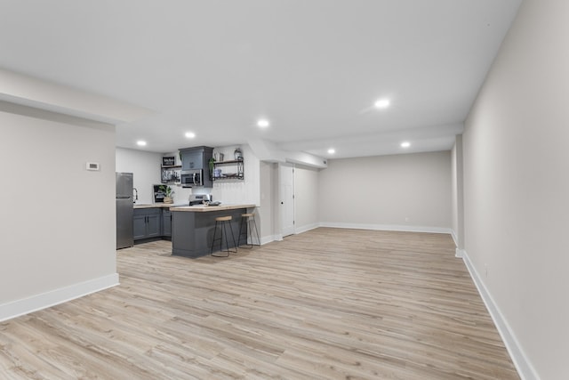 kitchen featuring a breakfast bar area, open shelves, stainless steel appliances, light wood-style flooring, and gray cabinetry