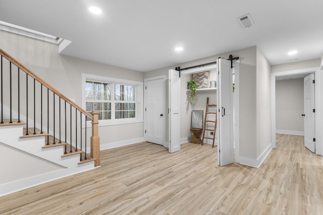 foyer featuring visible vents, stairway, a barn door, wood finished floors, and baseboards