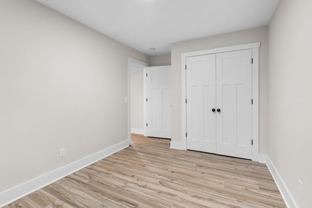 unfurnished bedroom featuring light wood-style flooring, baseboards, and a closet