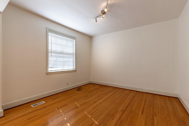 spare room with rail lighting, light wood-style flooring, visible vents, and baseboards