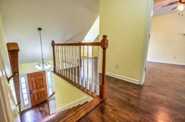 stairway featuring ceiling fan with notable chandelier, wood finished floors, baseboards, vaulted ceiling, and radiator