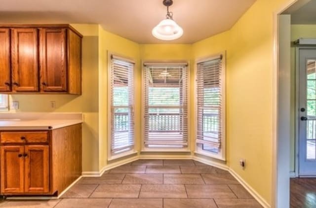 kitchen featuring baseboards, brown cabinets, light countertops, and decorative light fixtures