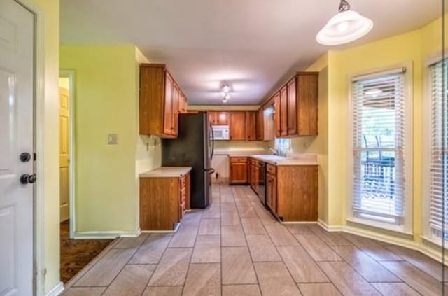 kitchen with dishwasher, white microwave, brown cabinets, freestanding refrigerator, and light countertops