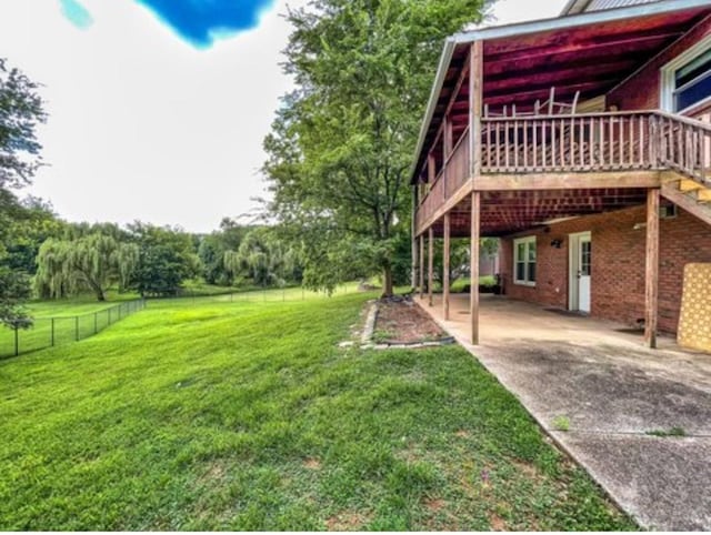 view of yard featuring an attached carport, driveway, a deck, and fence