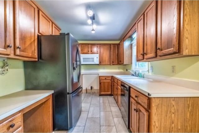 kitchen featuring white microwave, stainless steel fridge, brown cabinetry, and a sink