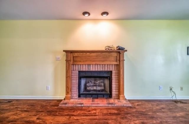 unfurnished living room with a brick fireplace, baseboards, and wood finished floors