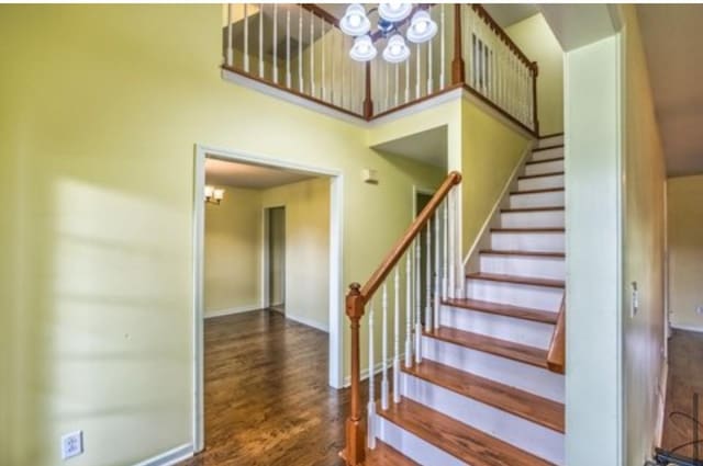 stairway with baseboards, wood finished floors, and a notable chandelier