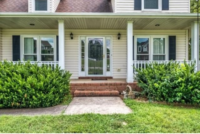 entrance to property featuring covered porch and roof with shingles